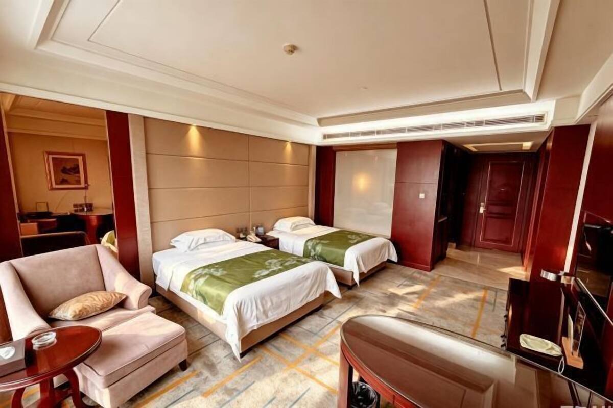 A hotel room with two beds, a sofa, a small table, and a TV.