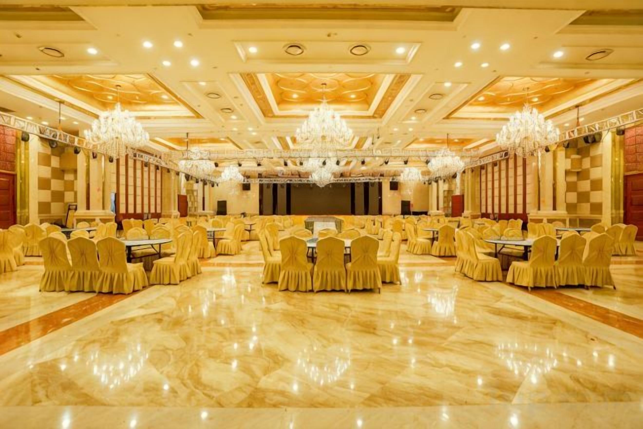 Um amplo salão de banquetes com fileiras de mesas e cadeiras, lustres e um palco.
