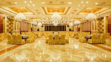 Um amplo salão de banquetes com fileiras de mesas e cadeiras, lustres e um palco.