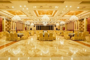 Un amplio salón de banquetes con filas de mesas y sillas, candelabros y un escenario.