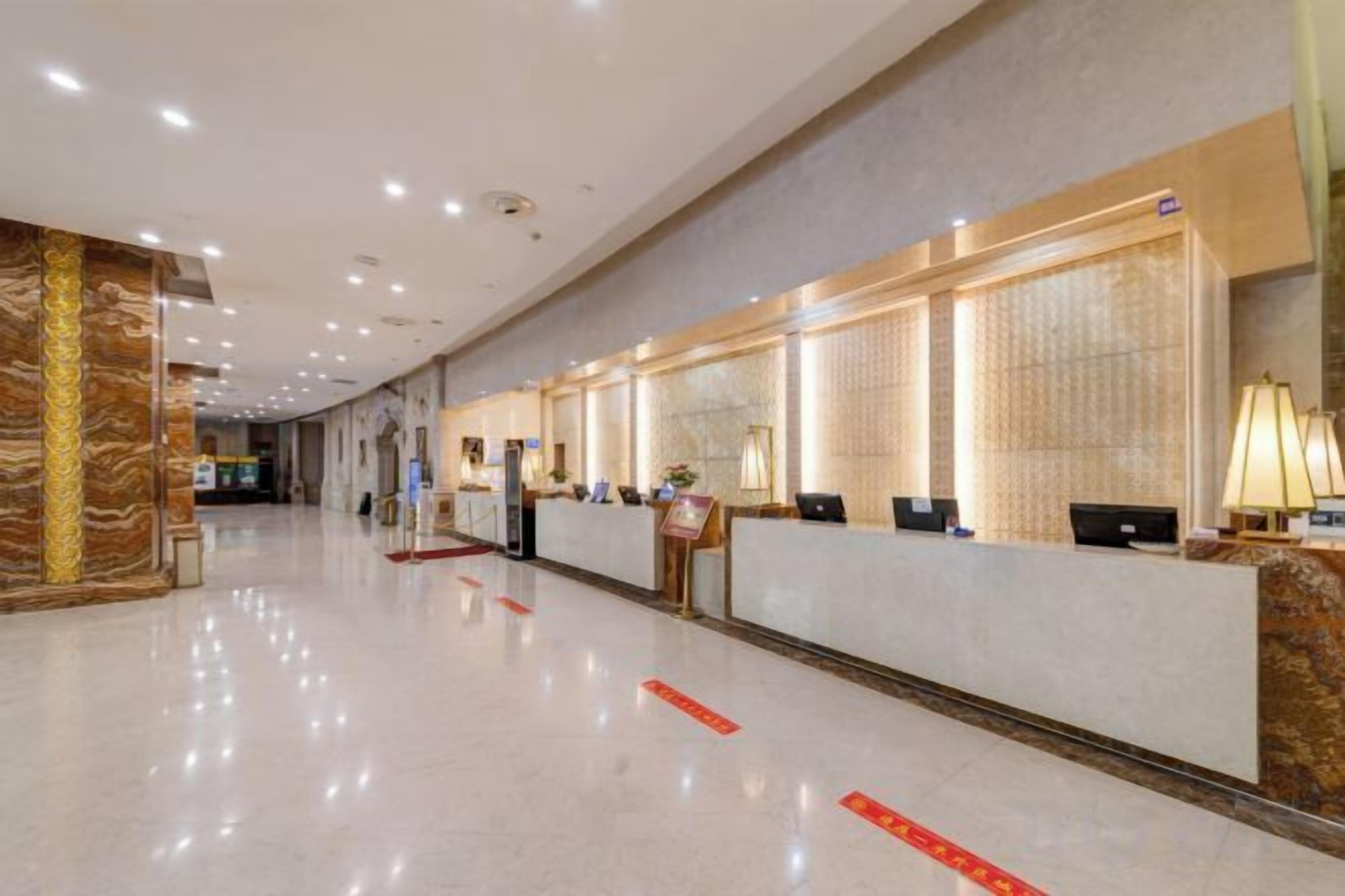 Un hall d’accueil d’hôtel avec un long comptoir de réception, plusieurs postes informatiques et un sol en marbre.