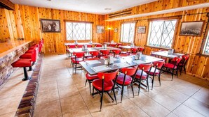 Ravintola, jossa on puuseinät, punaiset tuolit ja ruokailua varten katetut pöydät.