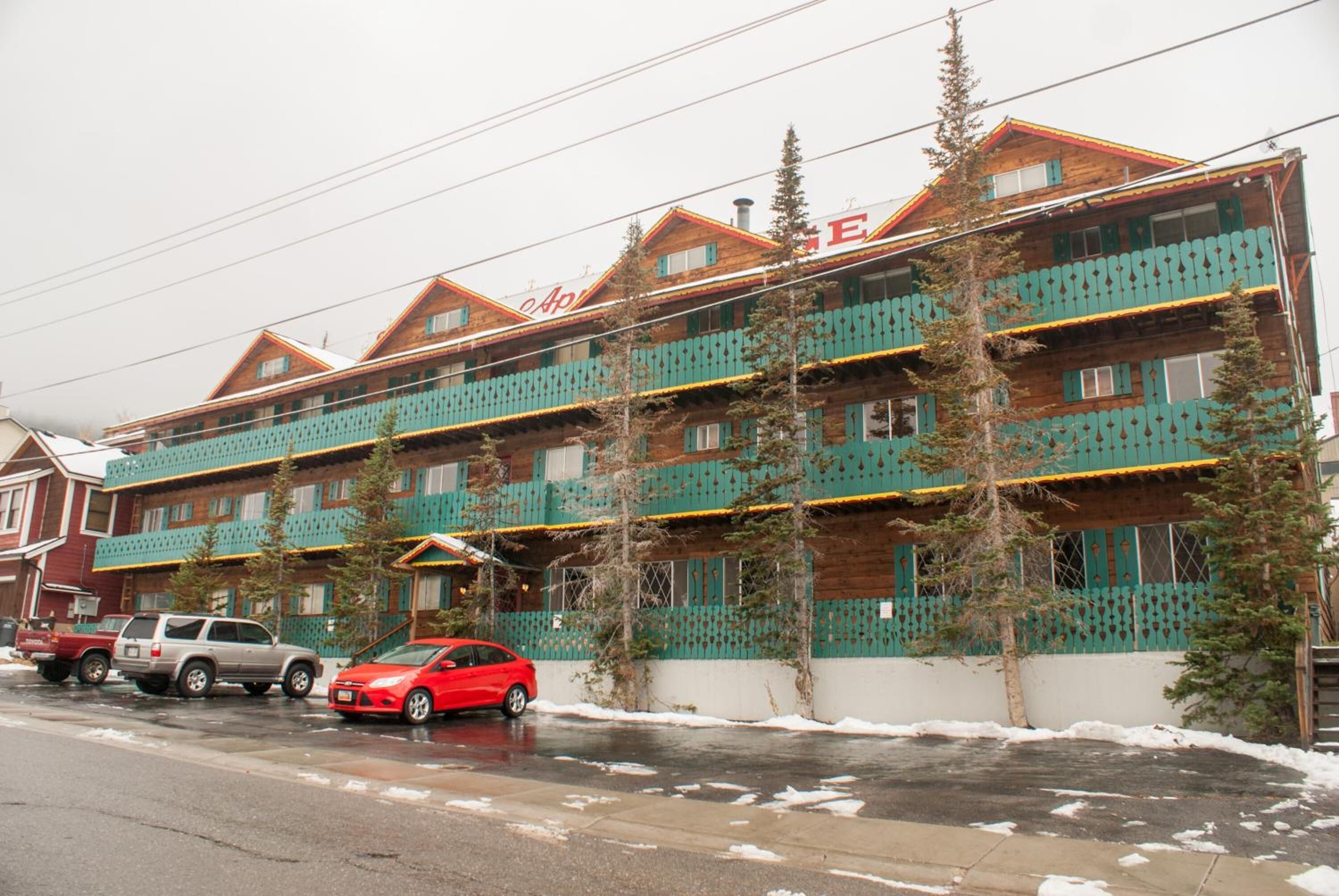 A multi-story hotel with a traditional wooden facade, balconies, and a red car parked in front.