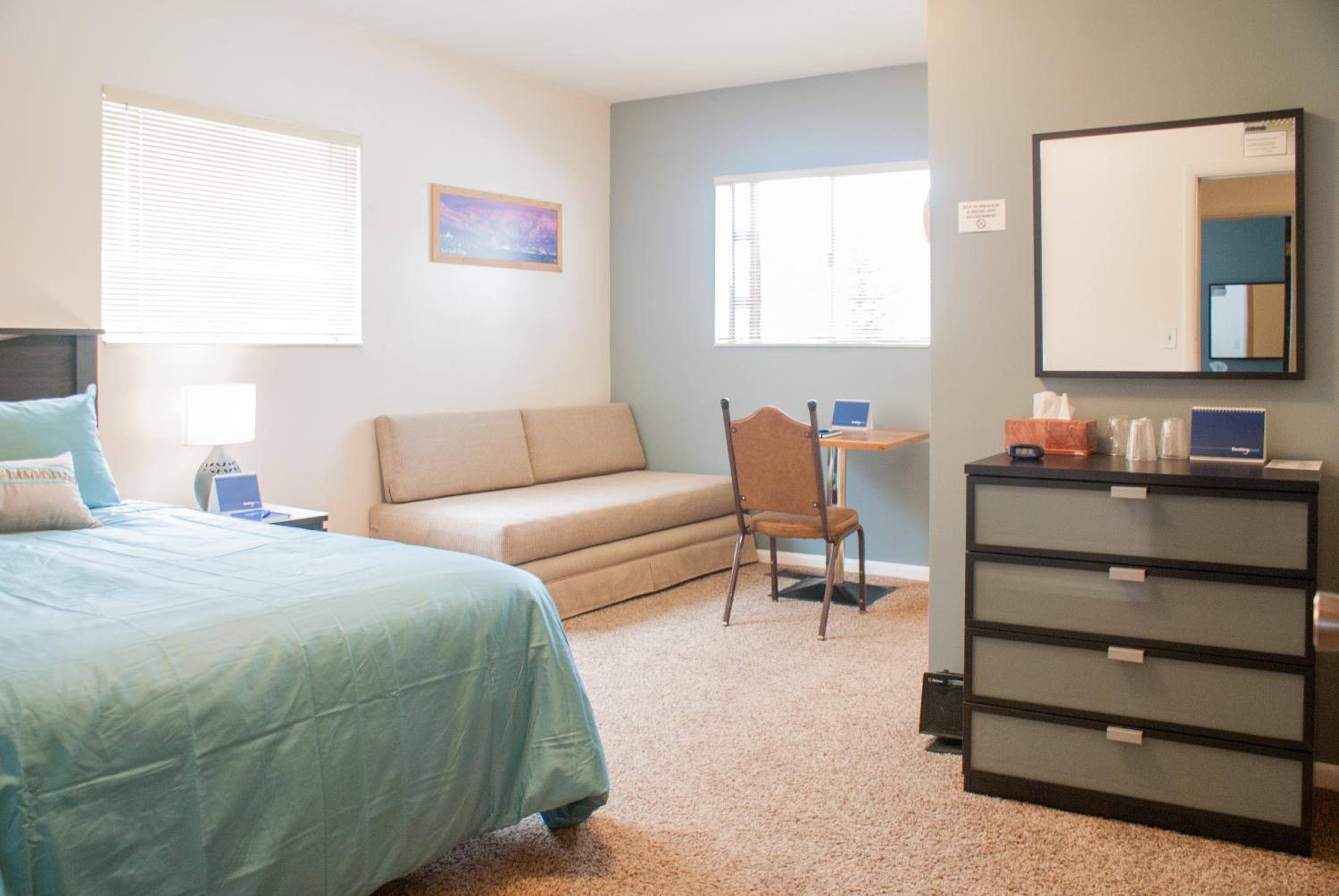 A bedroom with a bed, a desk, a chair, a dresser, and a window.
