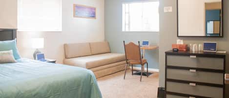 A bedroom with a bed, a desk, a chair, a dresser, and a window.