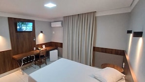 Una habitación de hotel con una cama, un escritorio con una silla, un televisor montado en la pared y una ventana con cortinas.