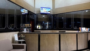 Un vestíbulo de hotel con un mostrador de recepción, un sofá y una pantalla de televisión que muestra una imagen de la propiedad.