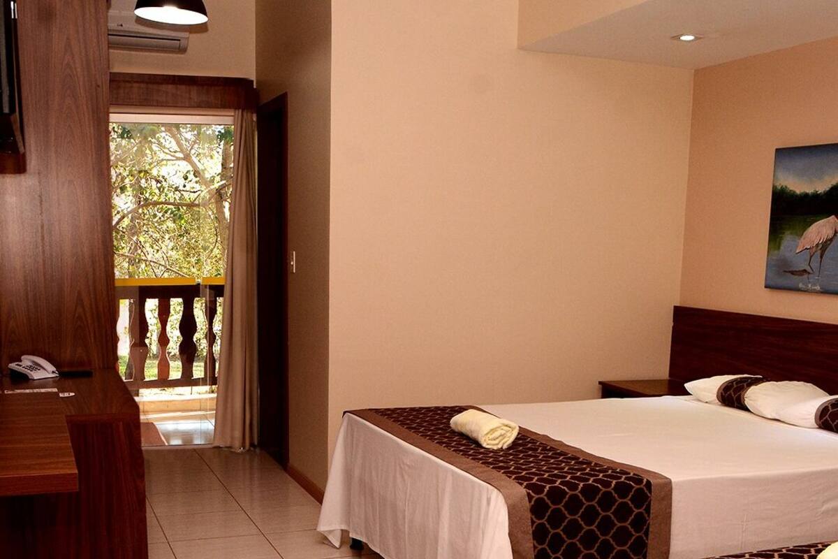 A hotel room with a bed, a desk, and a view of a balcony.