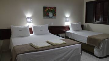 Quarto de hotel com duas camas, cada uma com roupa de cama e almofadas brancas, um quadro de flores na parede e duas luminárias de parede.