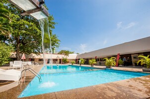 Una piscina con caída de agua, rodeada de sillas de descanso y plantas en macetas.