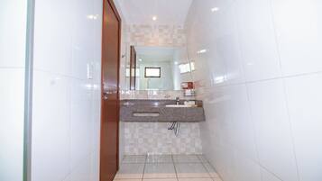Un baño estrecho con paredes de azulejos blancos, una puerta de madera, un lavamanos con espejo y una zona de ducha.