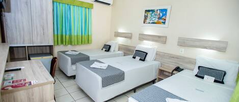 A hotel room with two beds, a desk, and a chair. There is a window with curtains, a painting on the wall, and an air conditioning unit.