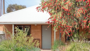 A house with a corrugated metal roof, a wooden door, and a small front porch. - Mud Hut Motel (Coober Pedy)