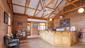 A reception area with a wooden counter, a desk, and a chair. There are informational cards on the wall and a fire extinguisher near the counter. - Mud Hut Motel (Coober Pedy)