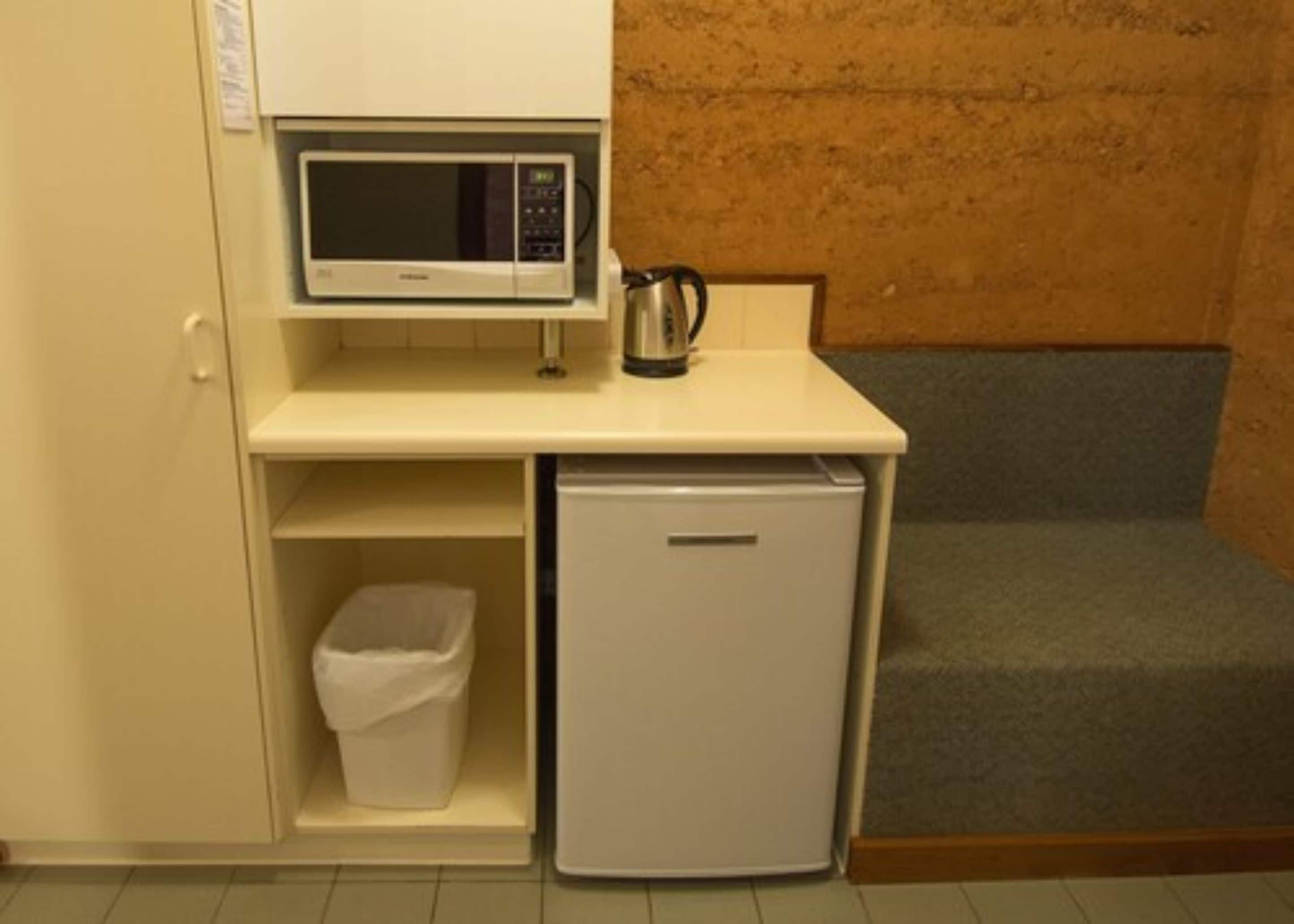 A kitchenette with a microwave, a small refrigerator, and a trash bin.