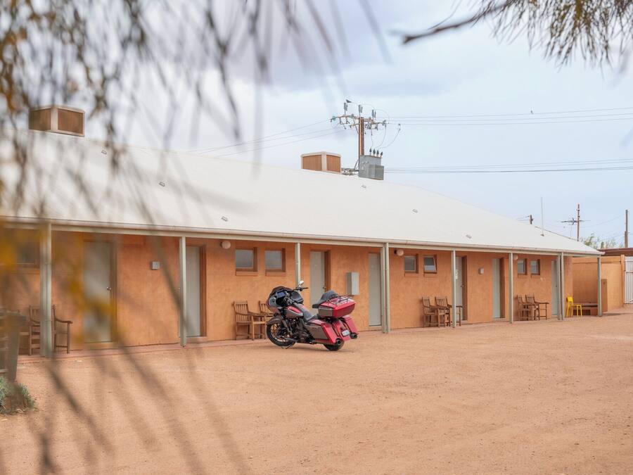 Edifici d'una sola planta amb teulada plana, una moto aparcada al davant i un sòl de terra.