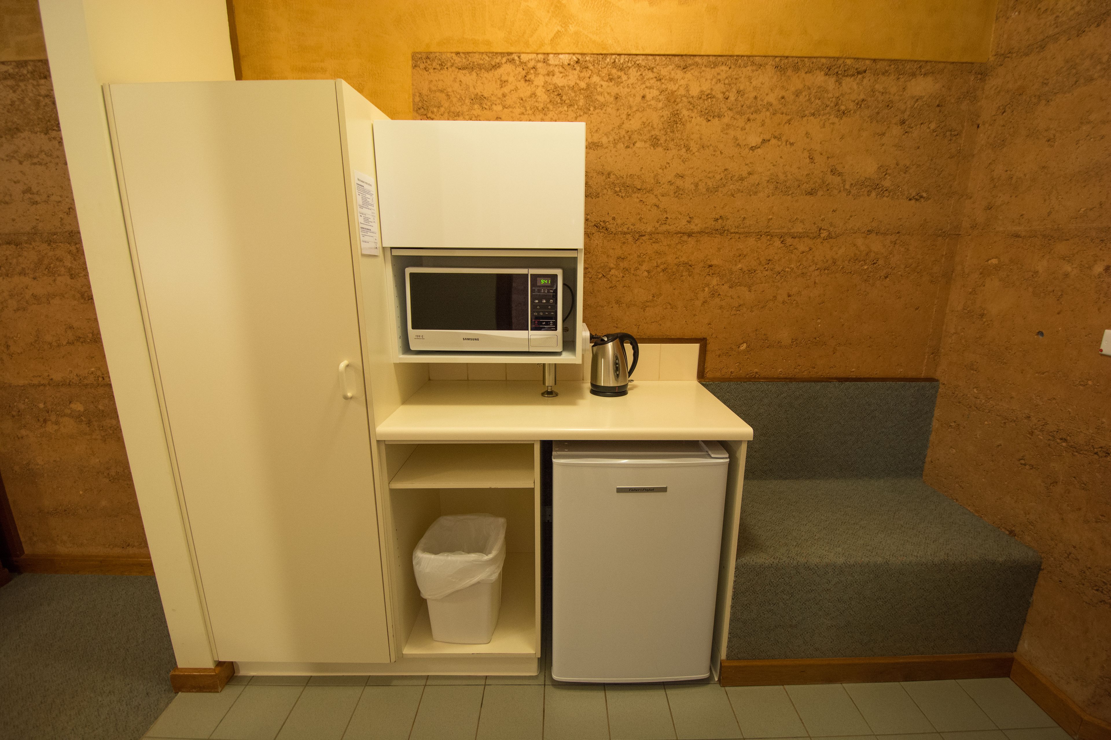 A compact kitchenette with a microwave, a small refrigerator, and a trash bin.