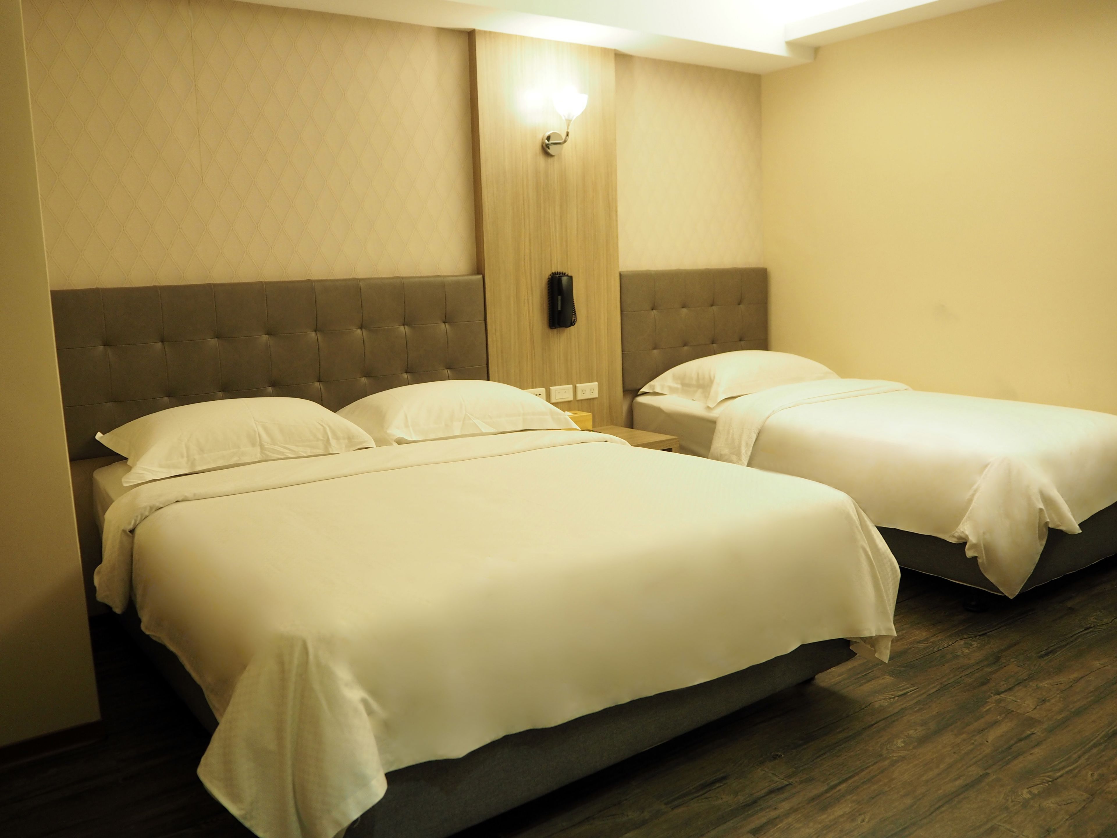 Habitación de hotel con dos camas, cabecera de madera, teléfono en la pared y lámpara.