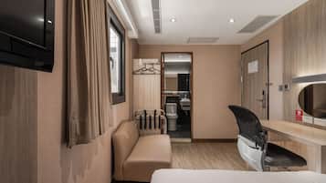 Quarto de hotel com cama, escrivaninha, poltrona, sofá, televisão e banheiro visível por uma porta aberta.