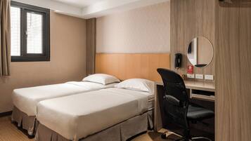 A hotel room with two single beds, a desk with a chair, a mirror, and a window with curtains.
