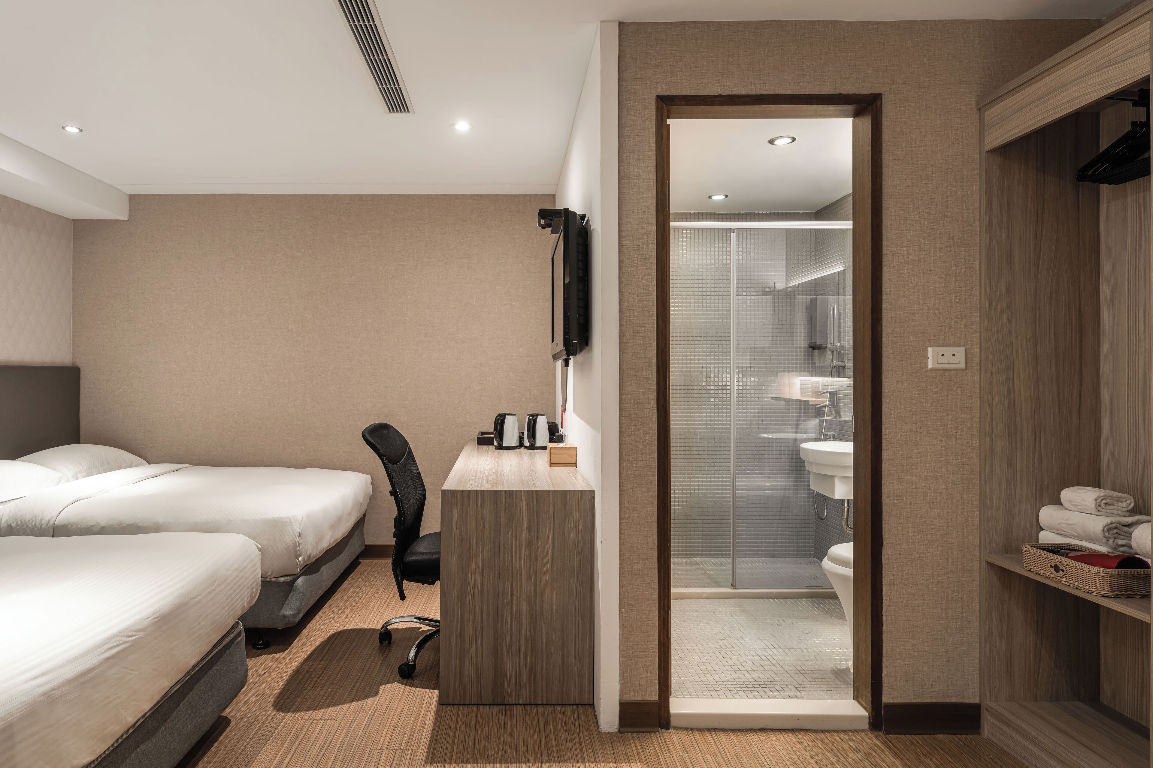 A hotel room with two beds, a desk, a chair, a TV, and a bathroom with a shower and toilet.