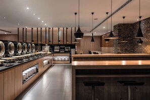 A modern kitchen with a long counter, black pendant lights, and a brick accent wall. - The Riverside Hotel International (Kaohsiung)