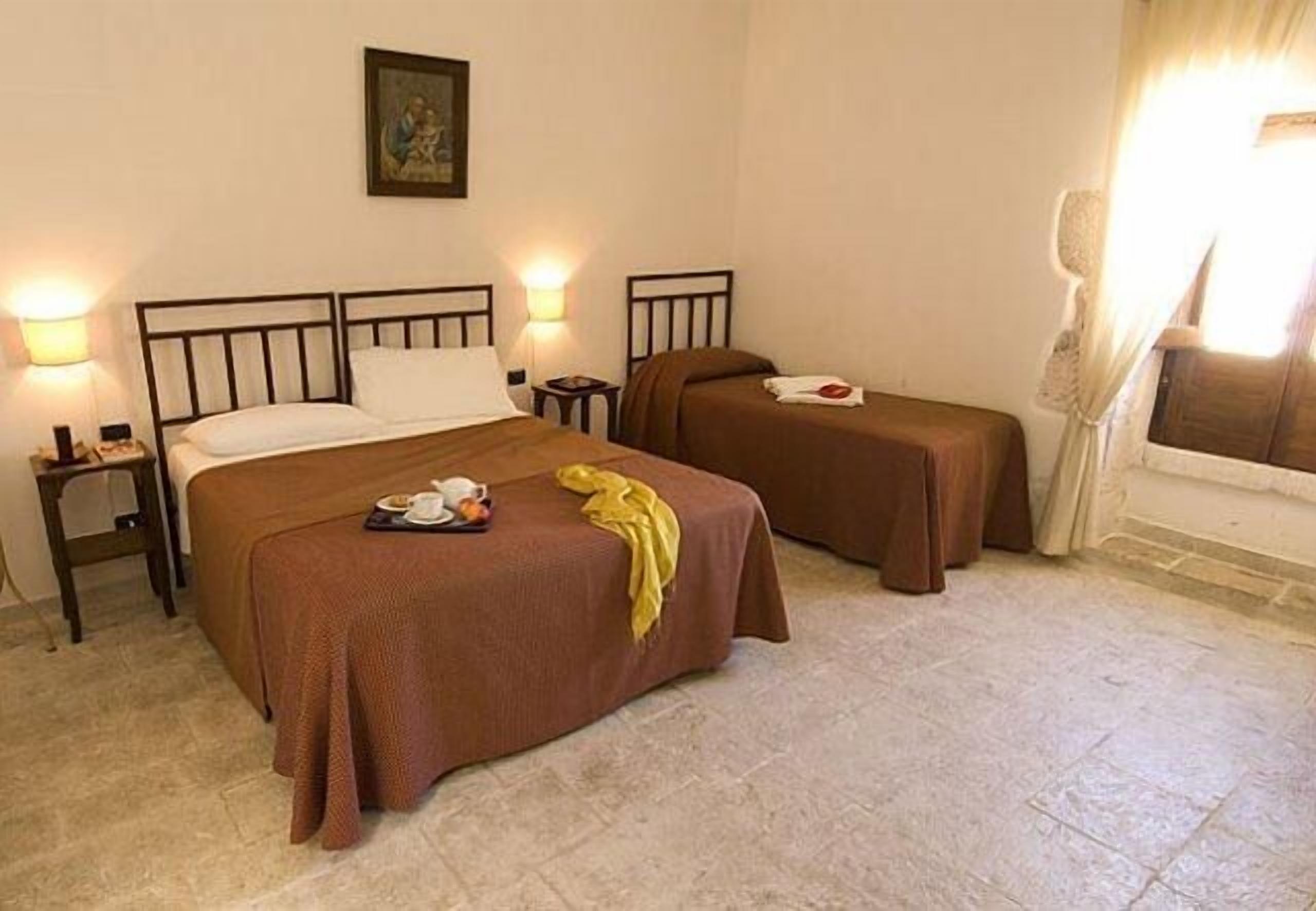 Habitación de hotel con dos camas individuales, una mesita de noche con lámpara, un cuadro en la pared y una ventana con cortinas.