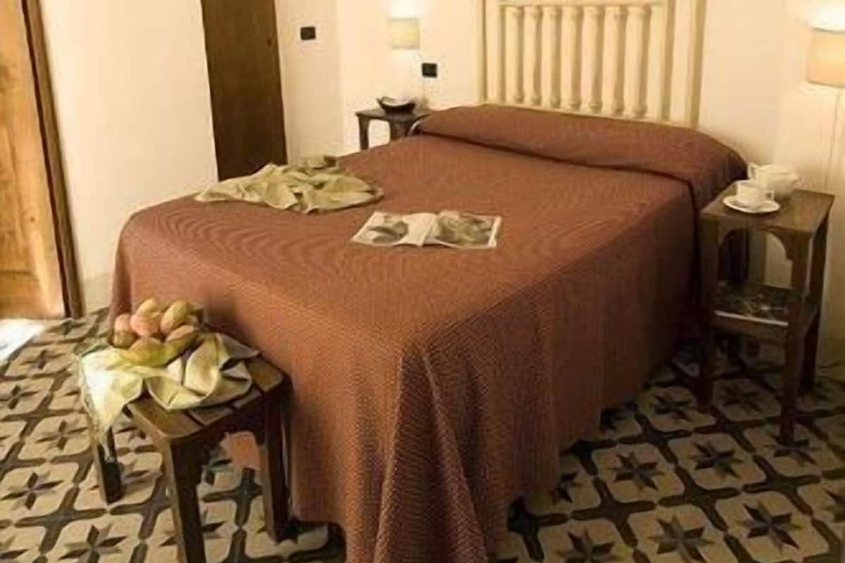 Una cama bien hecha con una colcha marrón, una mesita de noche con una lámpara y un suelo con diseño.