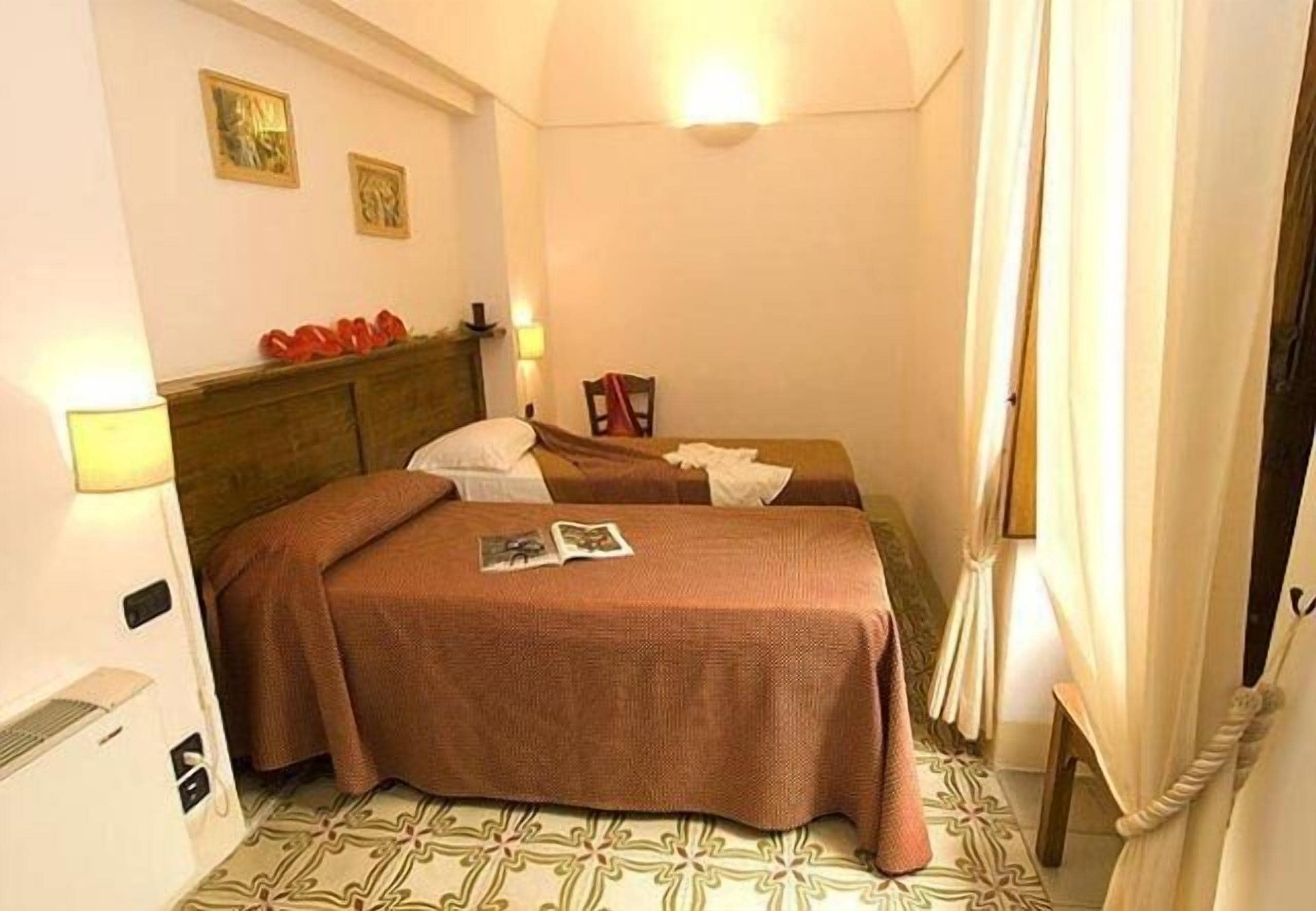 A hotel room with two beds, a headboard, wall-mounted lamps, and a patterned floor.
