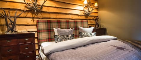 A bedroom with a plaid headboard, a wooden dresser, and antler wall decor.