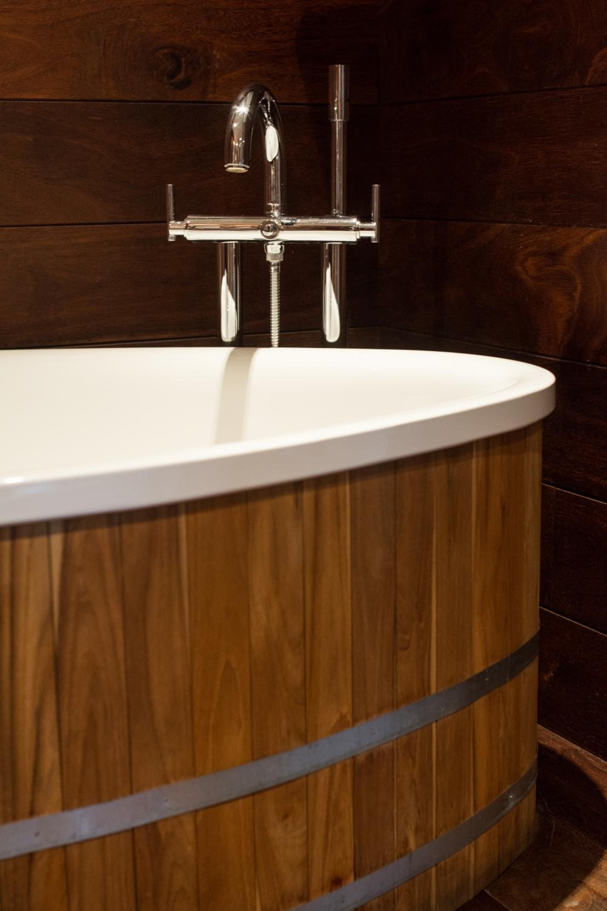 Une baignoire en bois avec un robinet chromé et une pomme de douche à commande unique.
