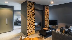 A modern living room with a fireplace, a sofa, a TV, and a large wooden log wall. - Bliss Boutique Hotel (Breda)