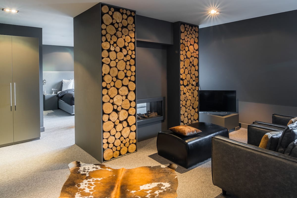 Ein modernes Wohnzimmer mit Kamin, einer Couch, einem Fernseher und einer großen Wand aus Holzstämmen.