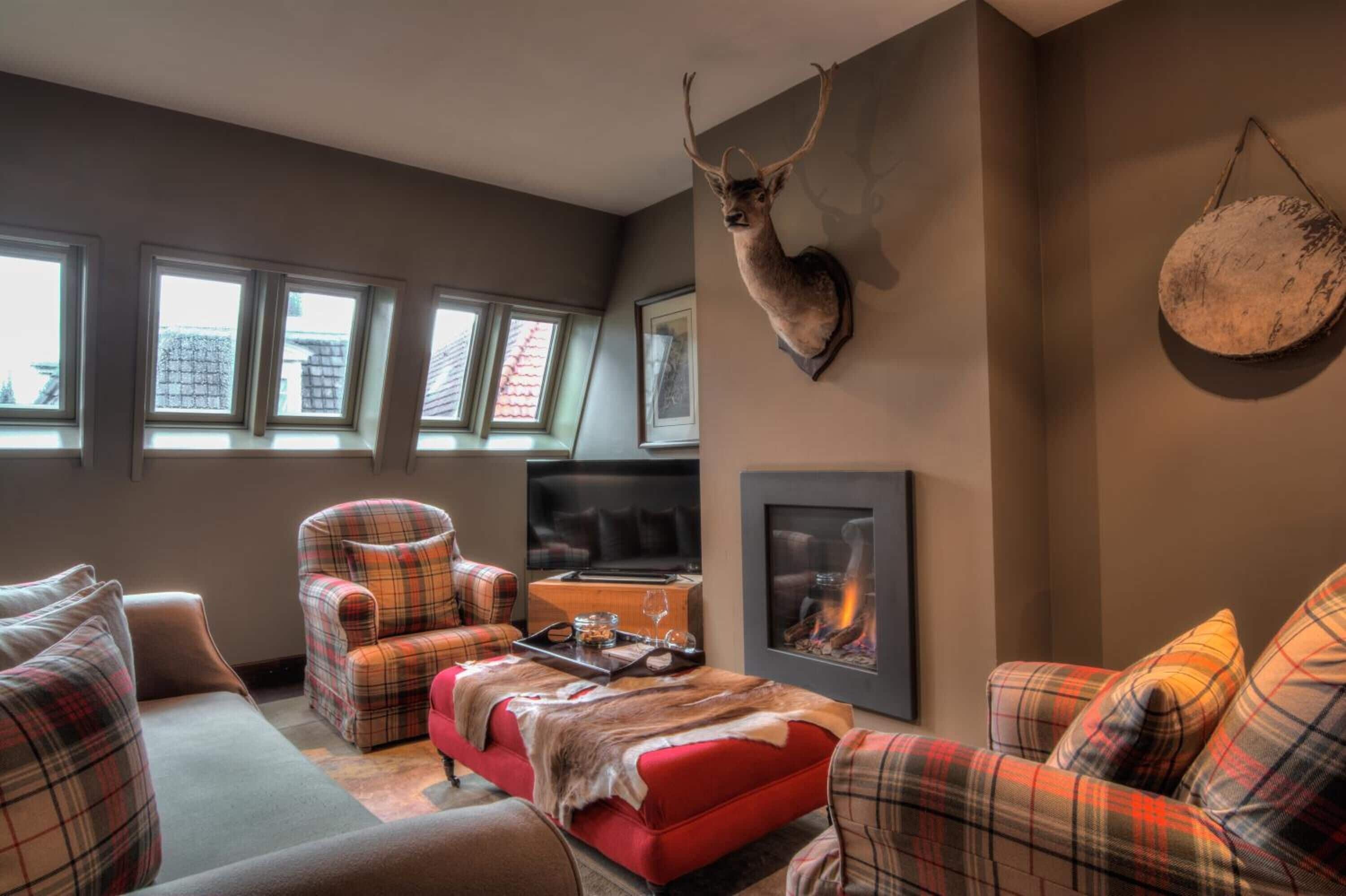 A cozy living room with plaid furniture, a mounted deer head, a fireplace, and a large window with multiple panes.