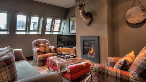 A cozy living room with plaid furniture, a mounted deer head, a fireplace, and a large window with multiple panes.