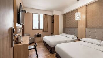 Habitación de hotel con dos camas, un escritorio con hervidor, una silla, televisor y ventana con cortinas.