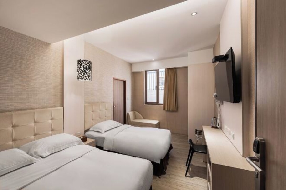 A hotel room with two beds, a desk, a chair, a TV, and a window with curtains.