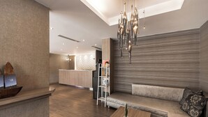 A modern interior with a wooden reception desk, a seating area with a sofa and a coffee table, a kitchen area, and a decorative chandelier. - The Riverside Hotel Hengchun (Hengchun)