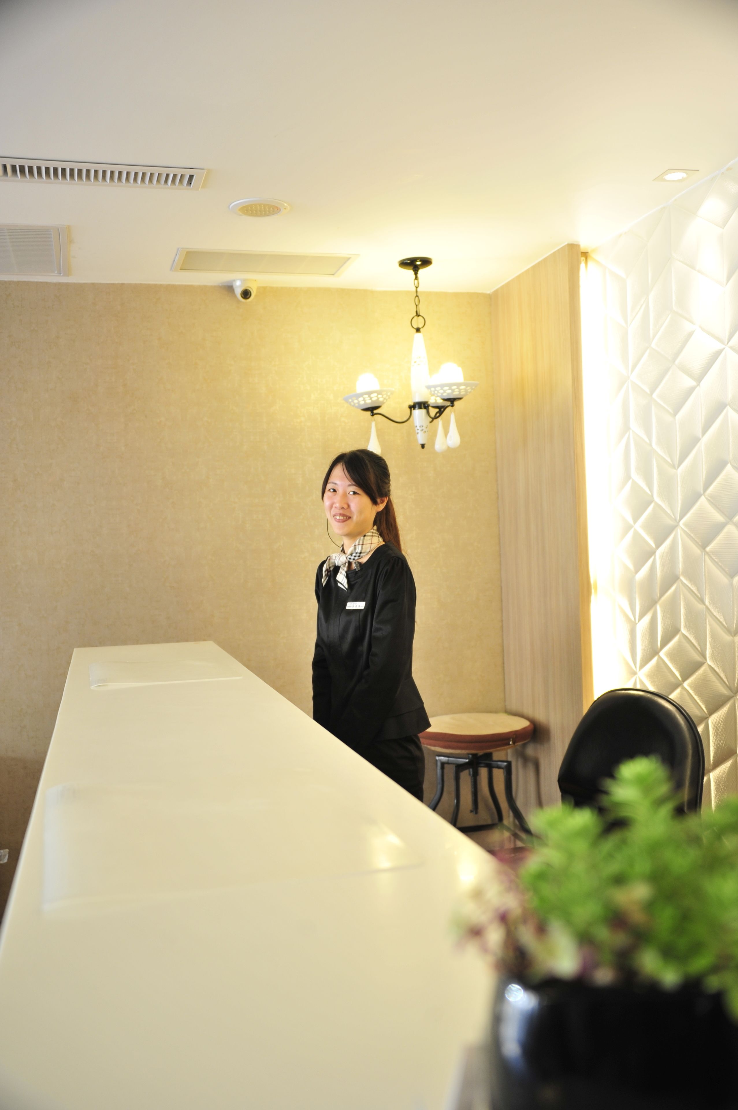 A person standing in a room with a long white table, a small round table, and a potted plant.