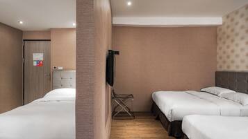 A hotel room with two beds, a wooden floor, a wall-mounted TV, and a door with a sign.