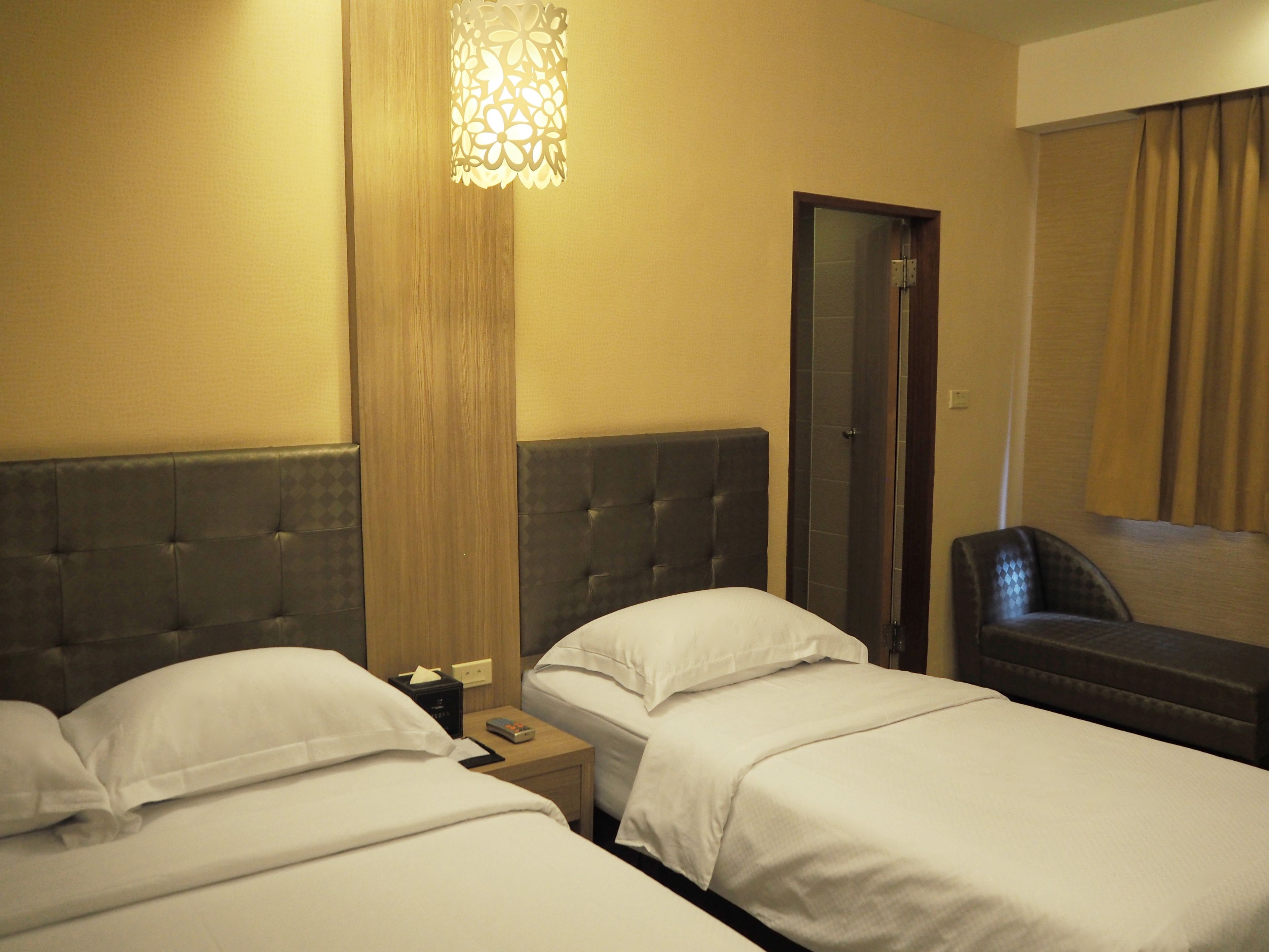 Habitación de hotel con dos camas, una mesita de noche, una lámpara y zona de ducha.