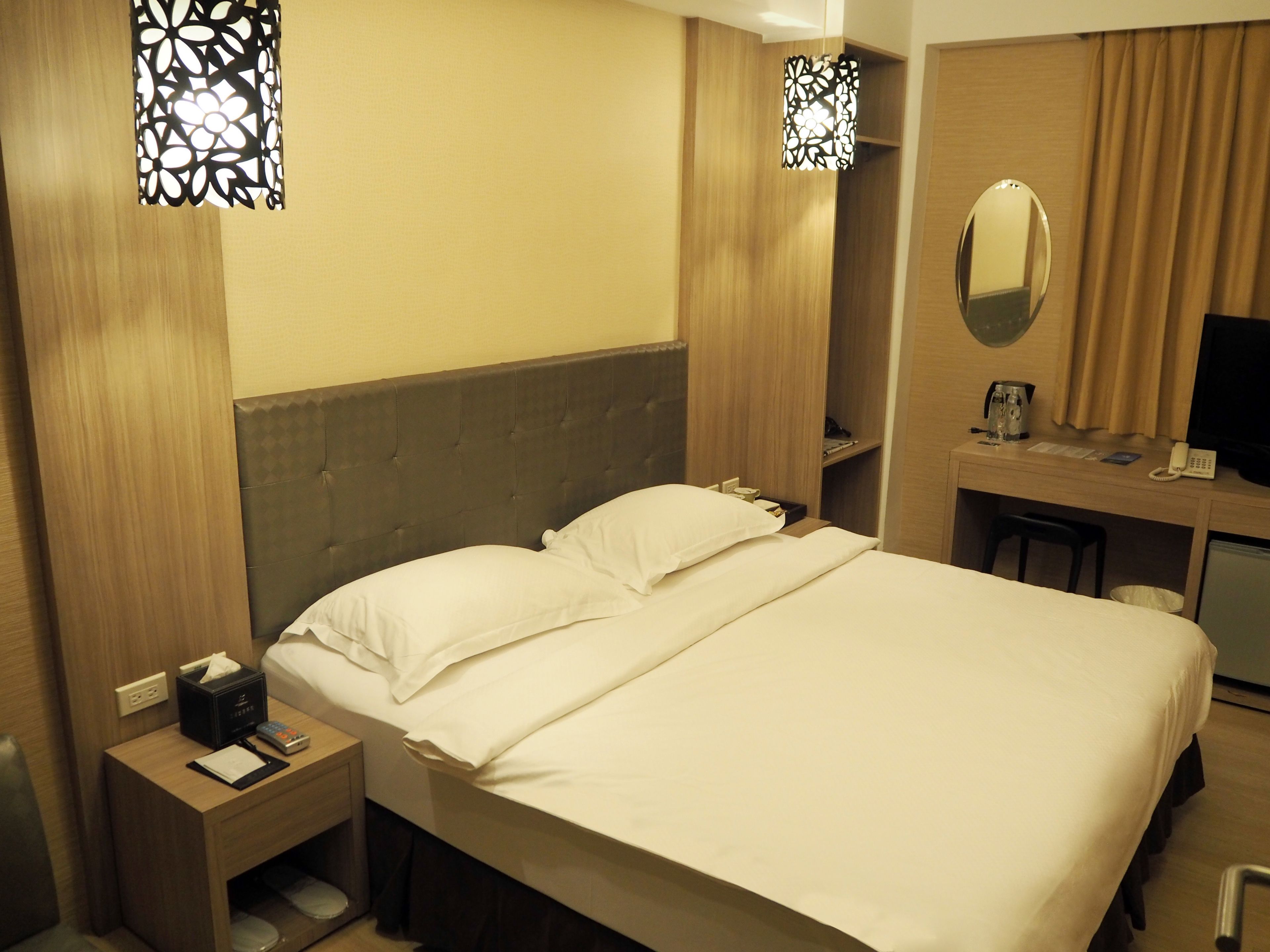 Habitación de hotel con una cama grande, mesitas de noche, un escritorio con silla, un espejo y una televisión.