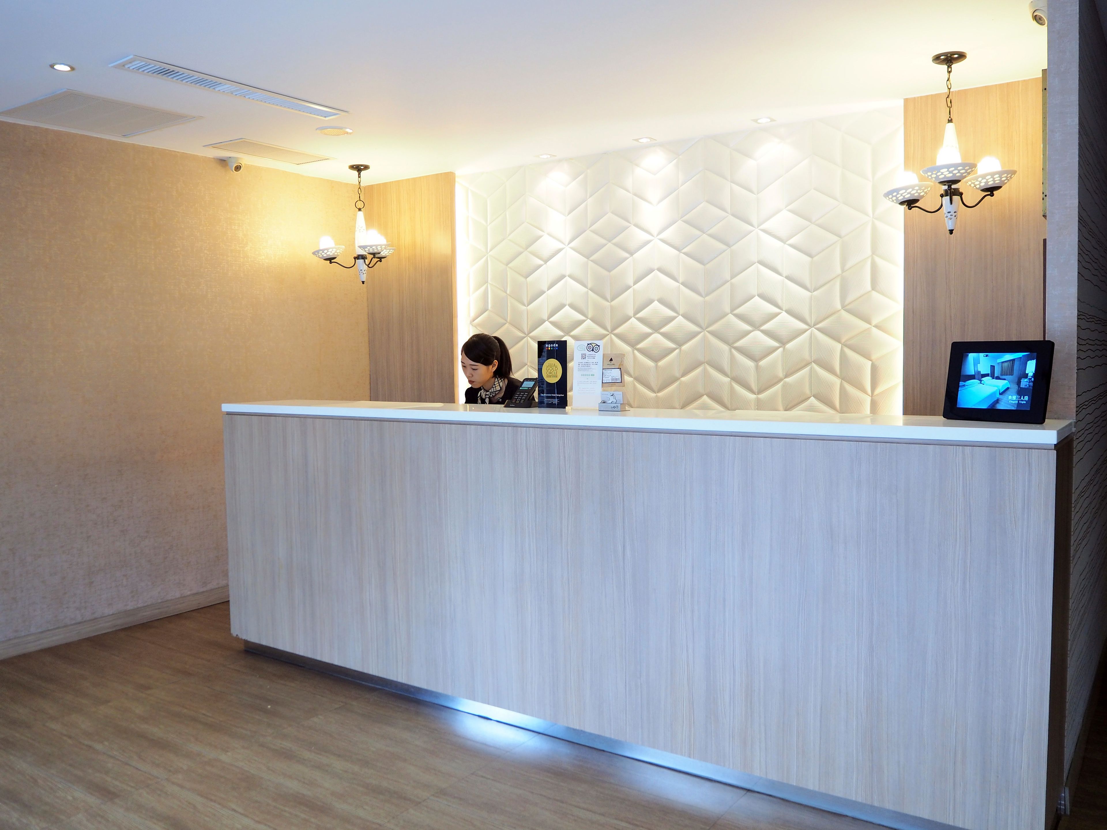 A reception desk with a modern design, a digital screen displaying a room, and a security camera above.