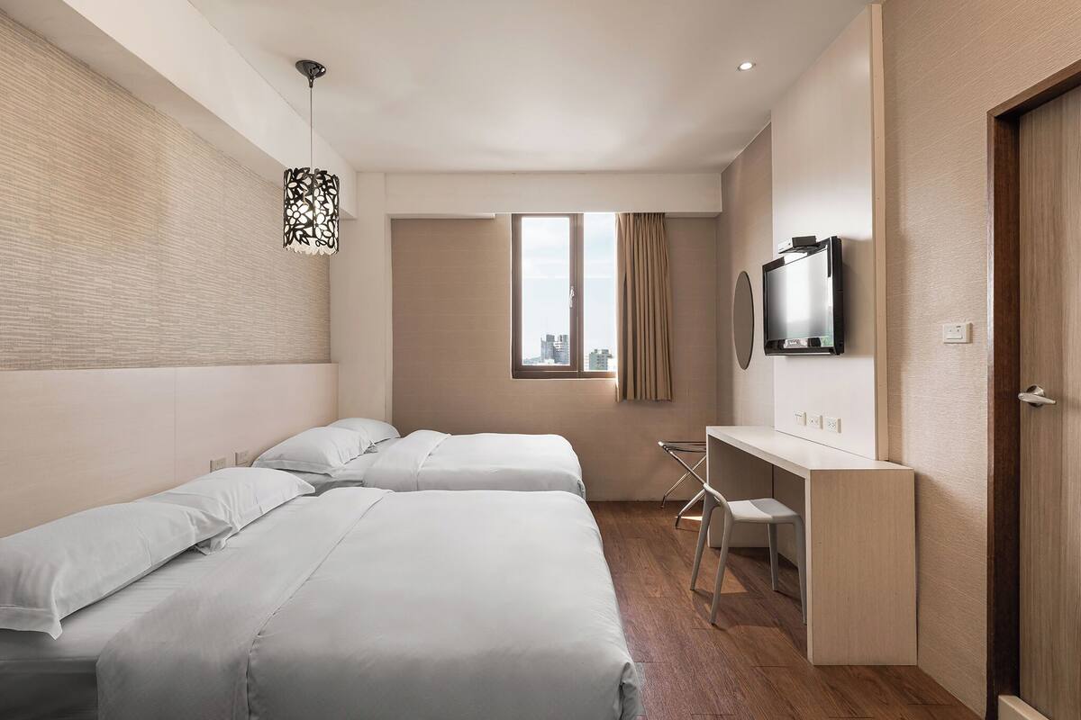 A modern hotel room with two beds, a desk, a television, and a window with curtains.
