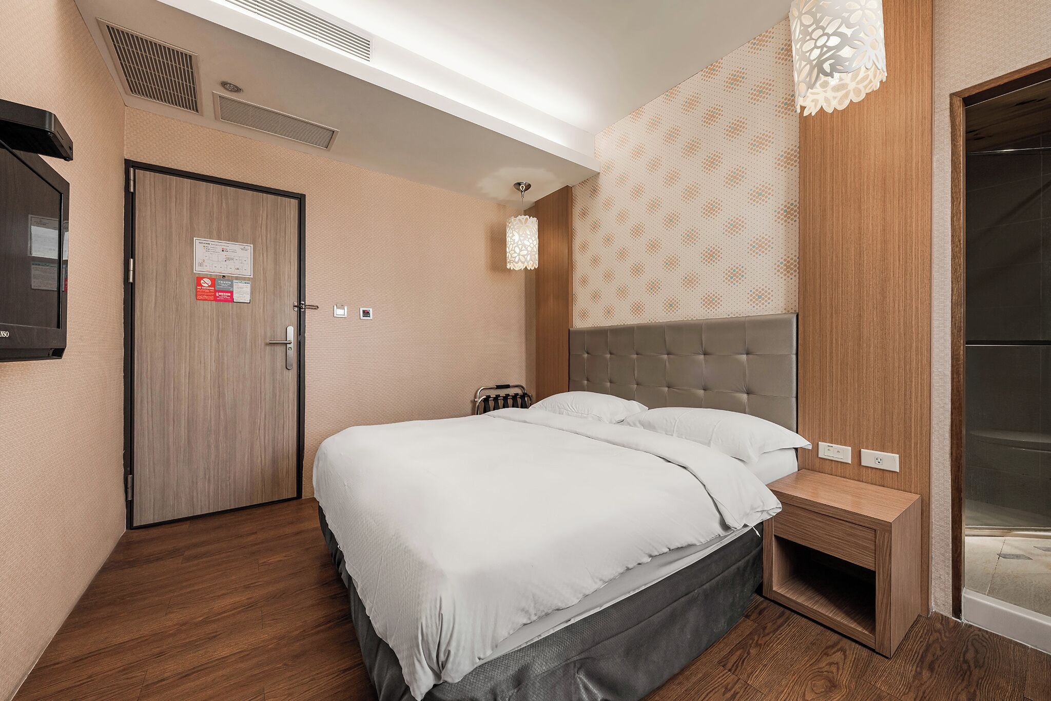 A modern hotel room with a large bed, a wooden nightstand, a TV, and a patterned wall.