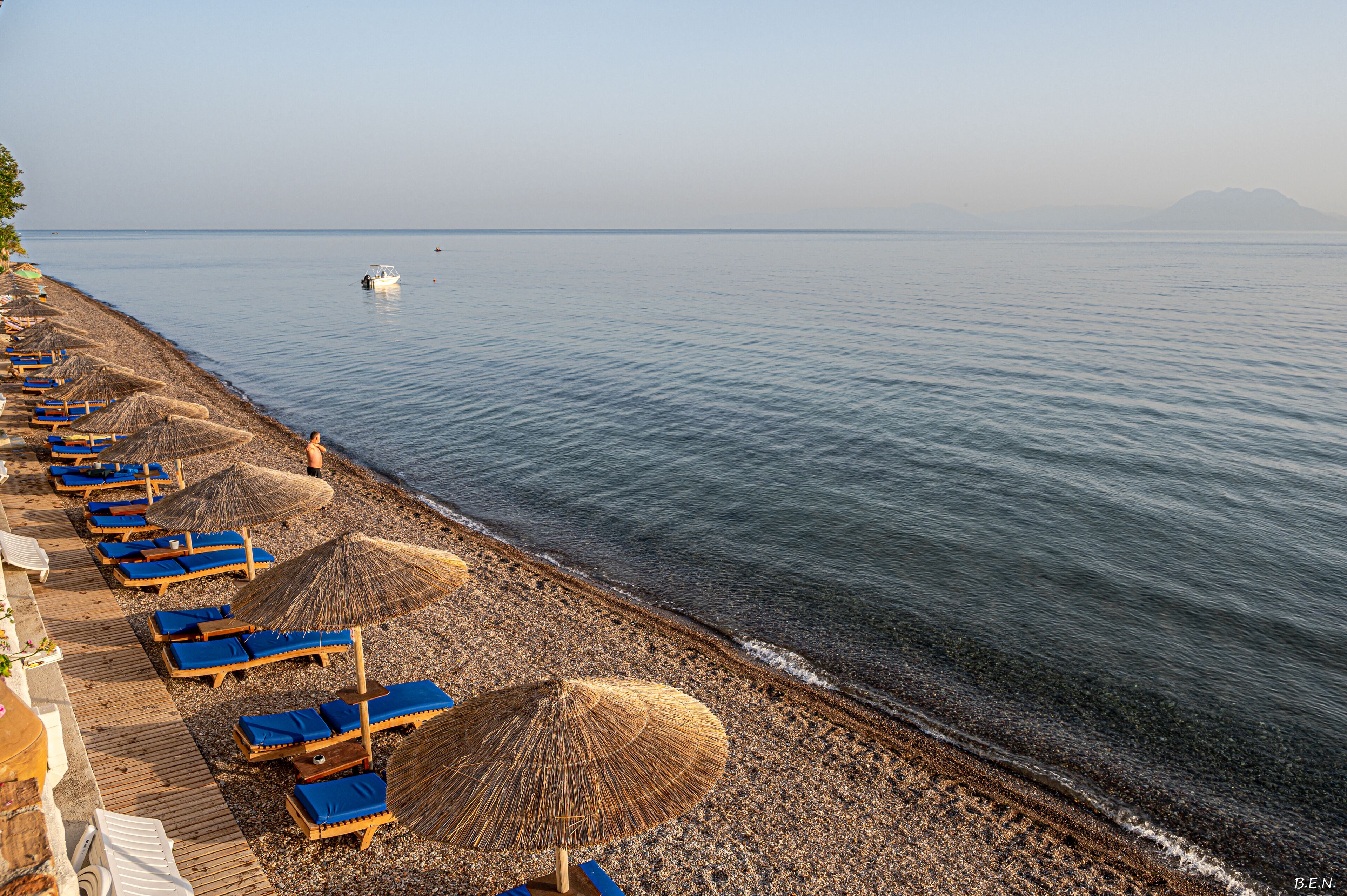 A beach with rows of sun loungers and thatched umbrellas along the shoreline.