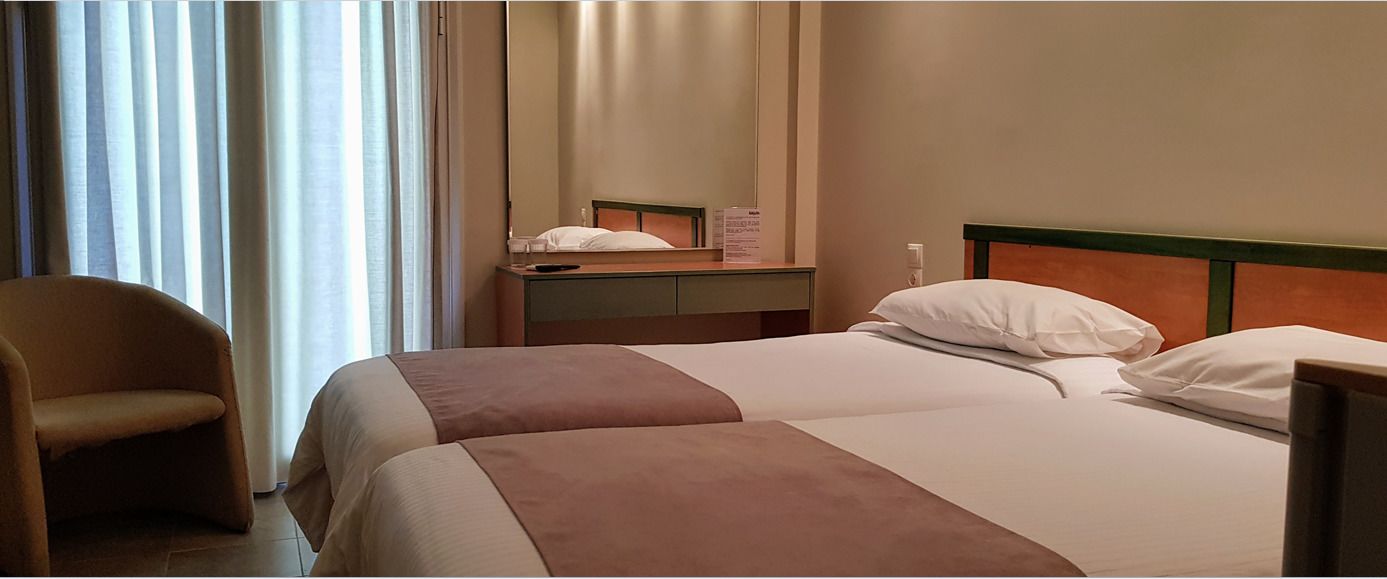 Habitación de hotel con dos camas, una silla, una mesita de noche y un espejo.