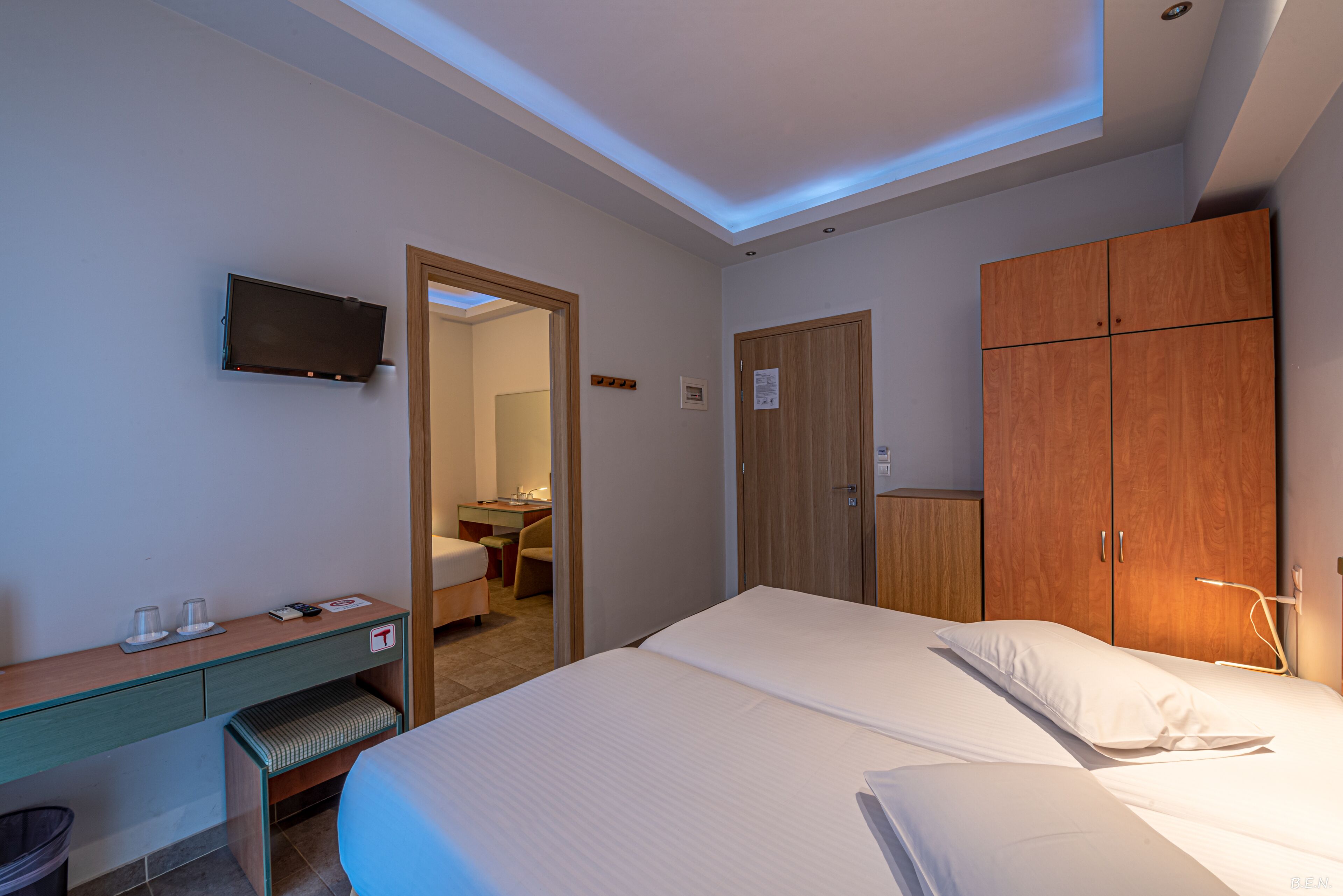 Una habitació d'hotel amb llit, escriptori, televisió i armari.