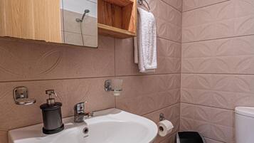 Ein Badezimmer mit weißem Waschbecken, einem Spiegel, einem Handtuchhalter, einer Toilette und einem Mülleimer.