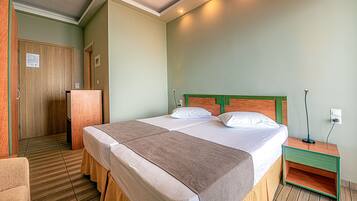 A hotel room with a double bed, a wooden wardrobe, a small bedside table, and a chair.